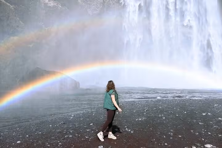 Woman standing before Skógafoss waterfall with double rainbow on Iceland's south coast