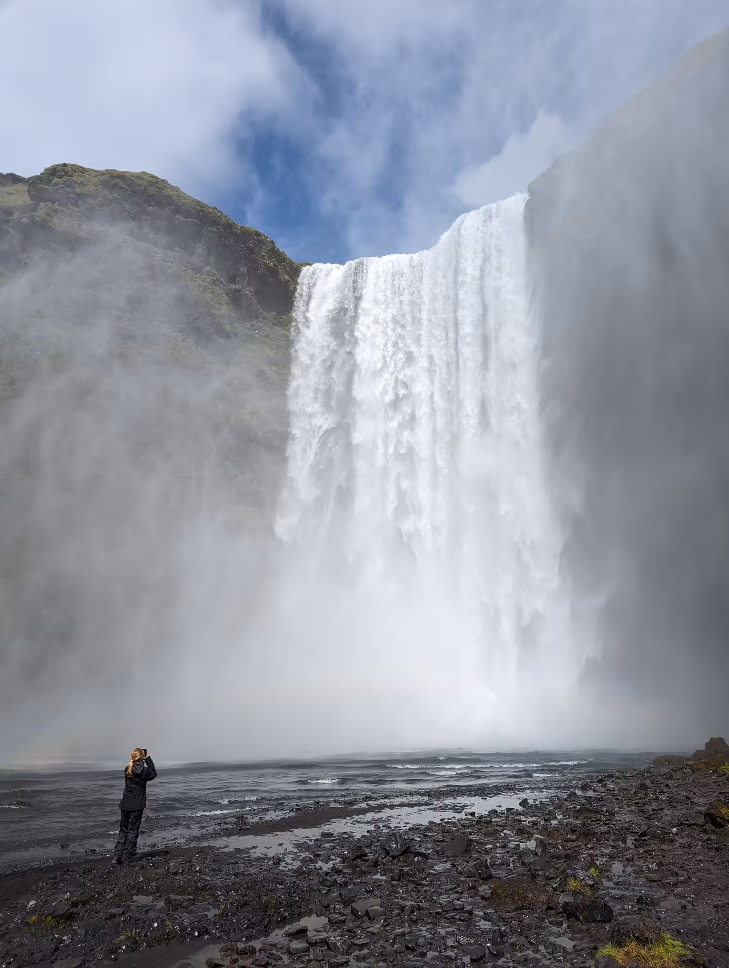 Hiker photographing massive Skógafoss waterfall with mist rising on Fimmvörðuháls trail in Iceland