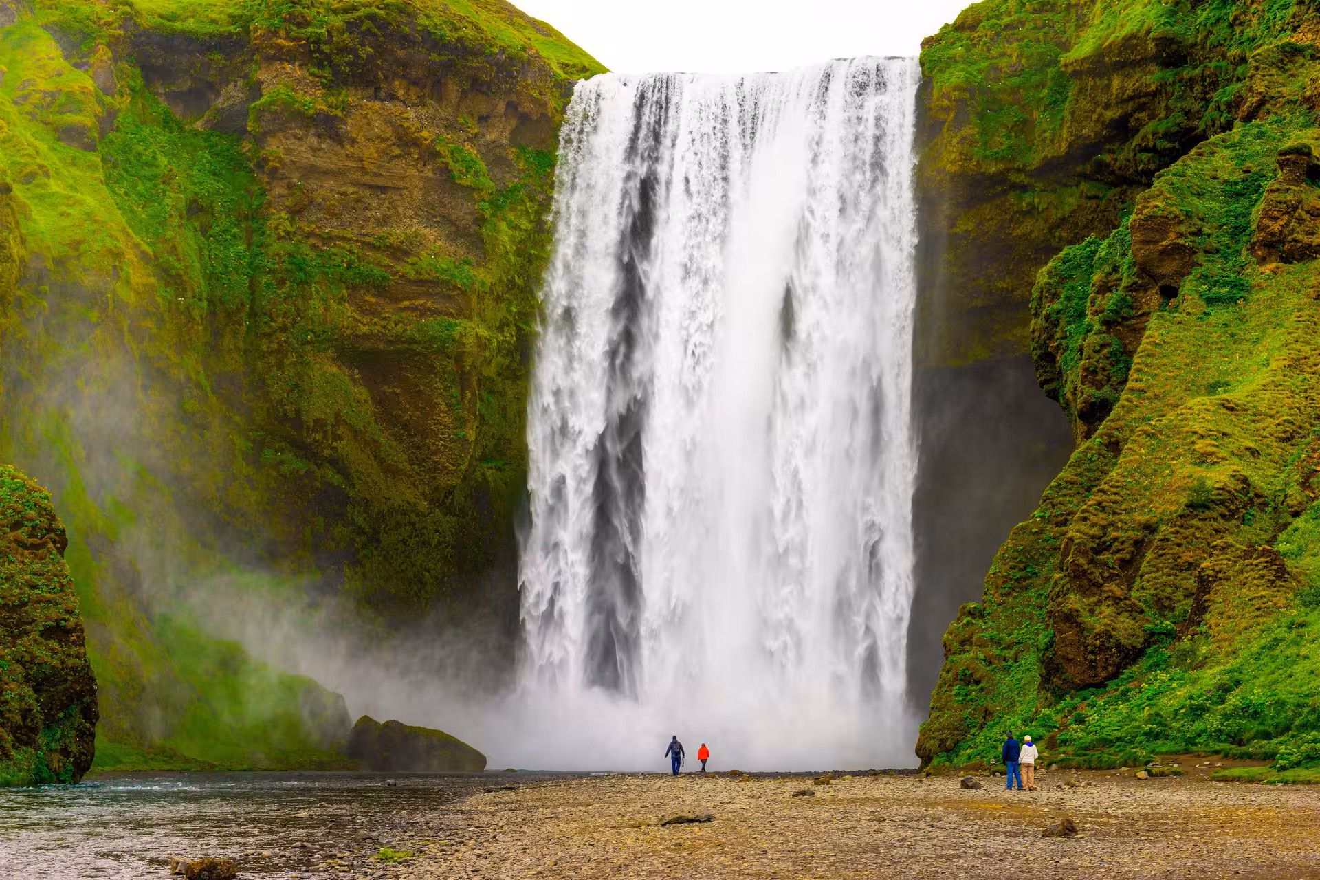 Majestic Skógafoss waterfall thundering down verdant cliffs, with visitors admiring its powerful beauty in Iceland.