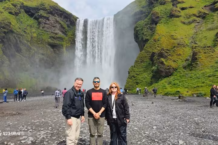 Three tourists posing in front of Skógafoss waterfall on Iceland's South Coast day tour