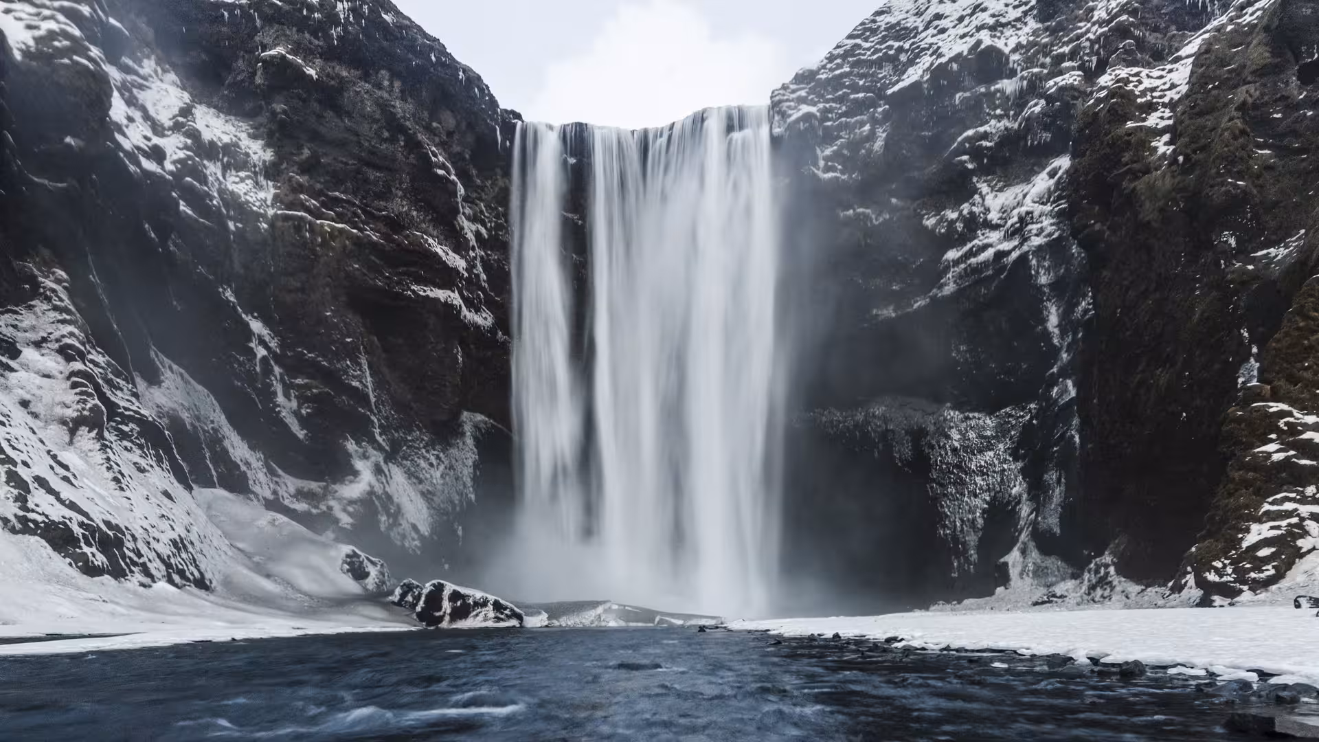 Skógafoss waterfall cascading over snow-covered cliffs on Iceland's South Coast in winter