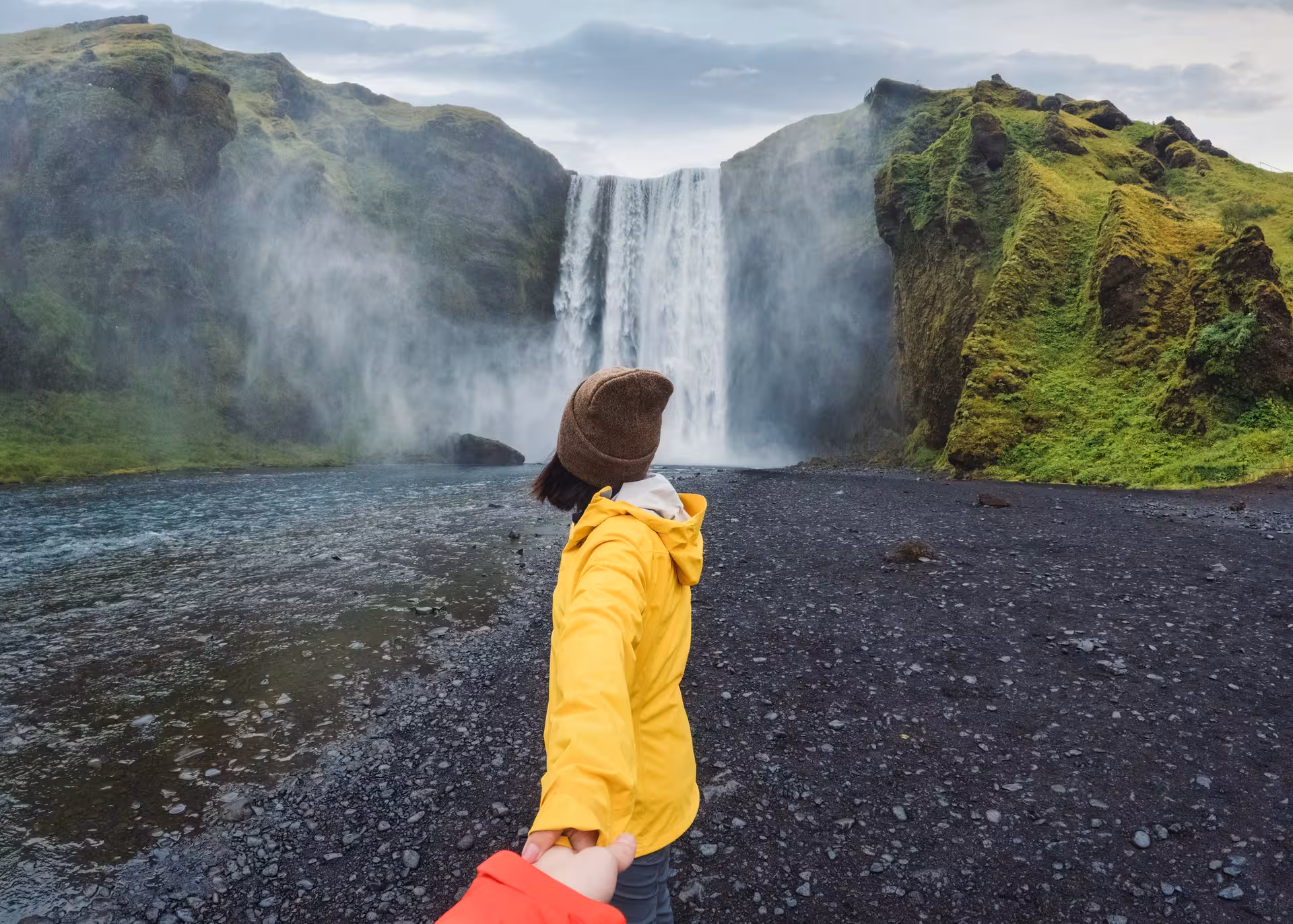Traveler in yellow jacket holding hands near Skógafoss waterfall on Iceland's South Coast