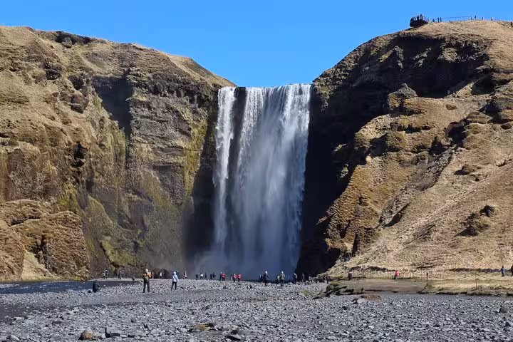 Massive Skógafoss waterfall on Iceland's south coast with tourists standing on rocky black terrain below