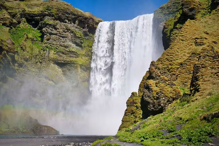Skógafoss waterfall cascading down mossy cliffs on Iceland's South Coast with rainbow mist