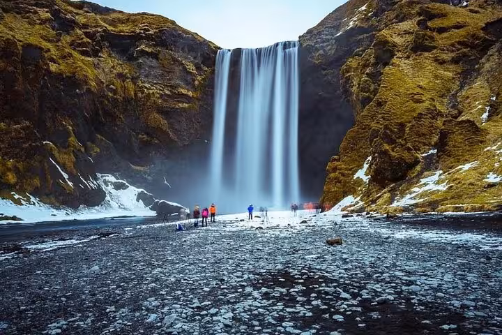Tourists standing before Skógafoss waterfall on Iceland's South Coast in winter with snow-covered ground