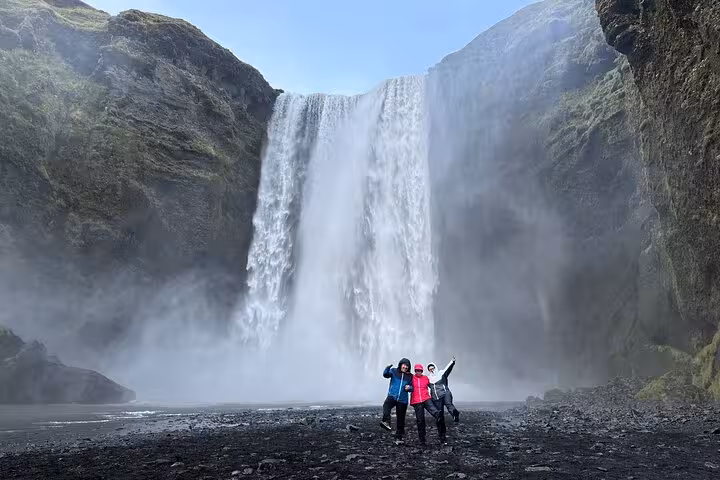Three tourists posing in front of Skógafoss waterfall on Iceland's South Coast tour