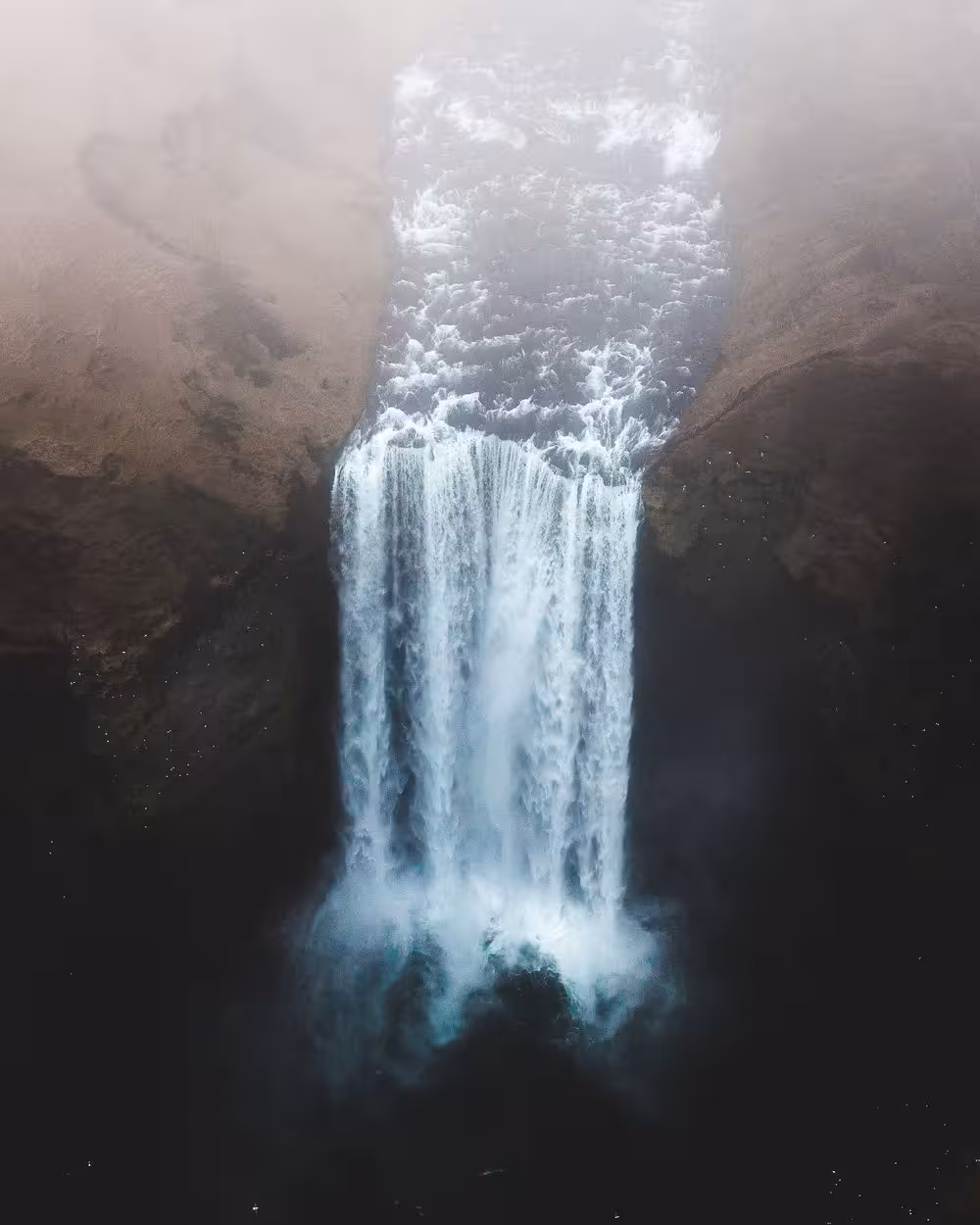 Aerial view of Skógafoss waterfall cascading down rocky cliffs into misty pool, Iceland South Coast