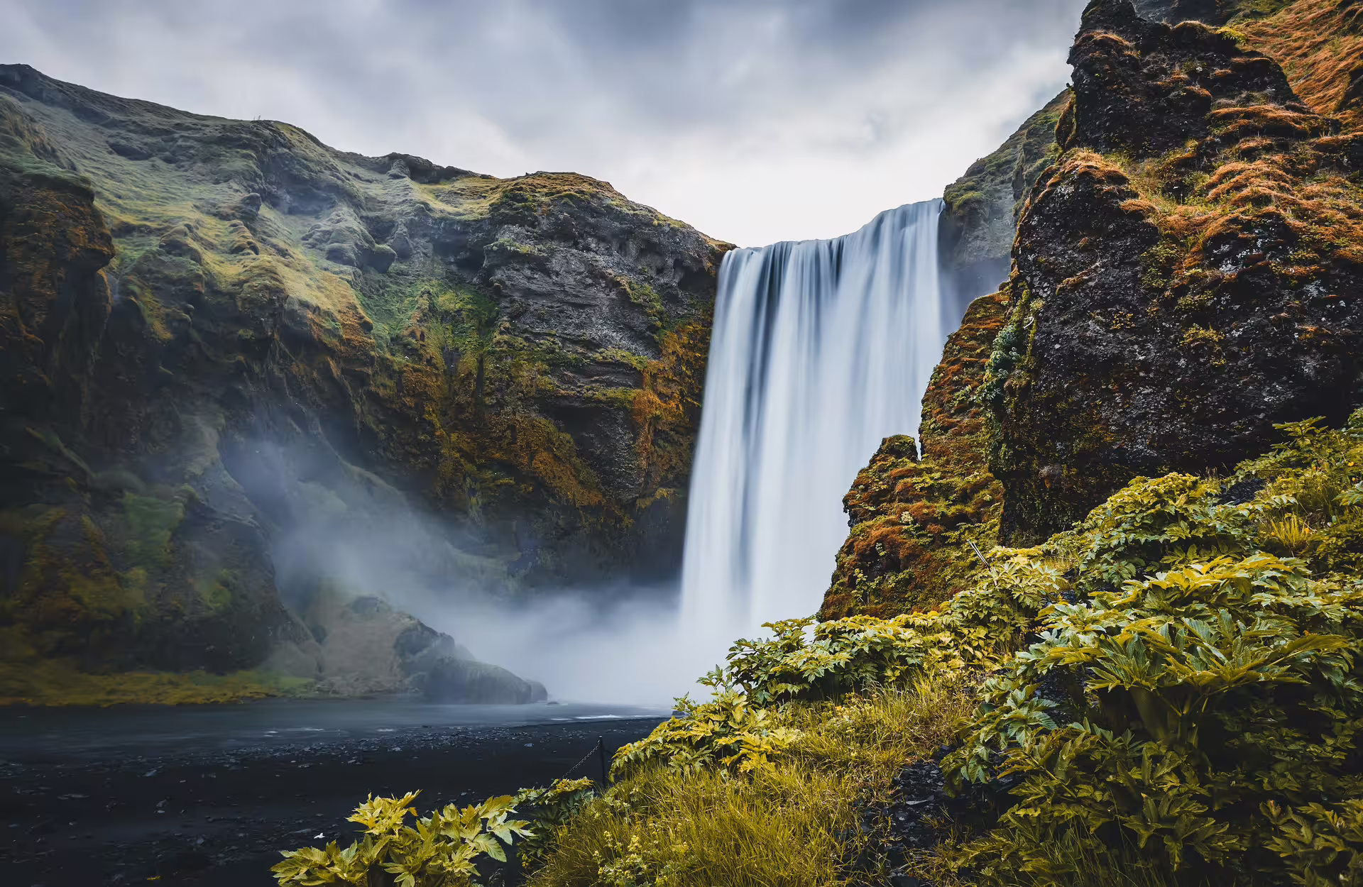 Skógafoss waterfall cascading down mossy cliffs on Iceland's South Coast with mist and lush green vegetation