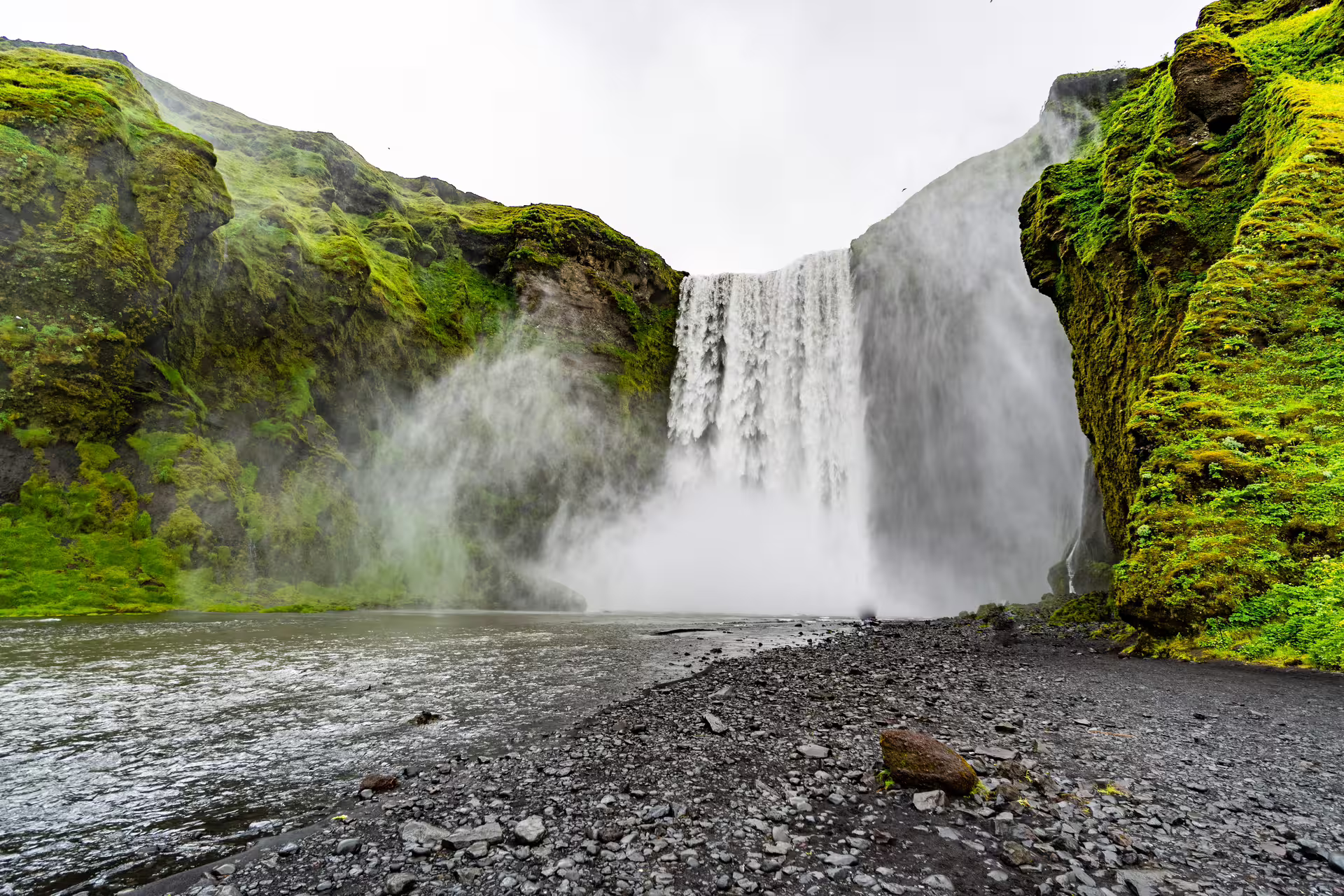 Skógafoss waterfall cascading down mossy cliffs on Iceland's south coast with black rocky shore
