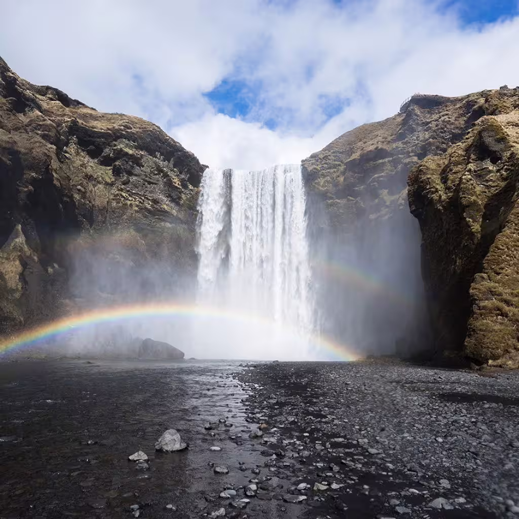 Skógafoss waterfall with rainbow over black rocky pool on Iceland's South Coast