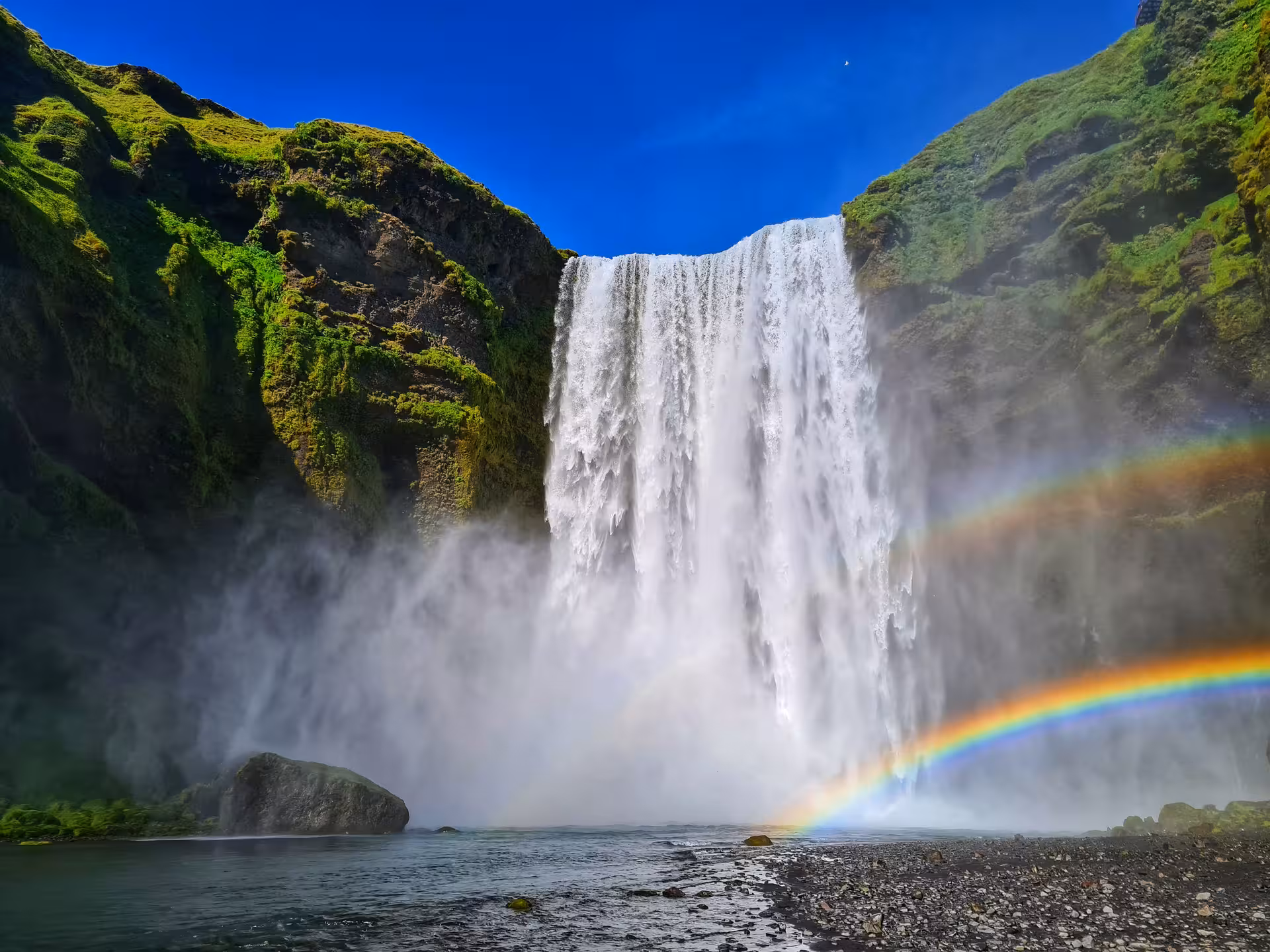 Skógafoss waterfall with rainbow and mist on Iceland's South Coast under blue sky