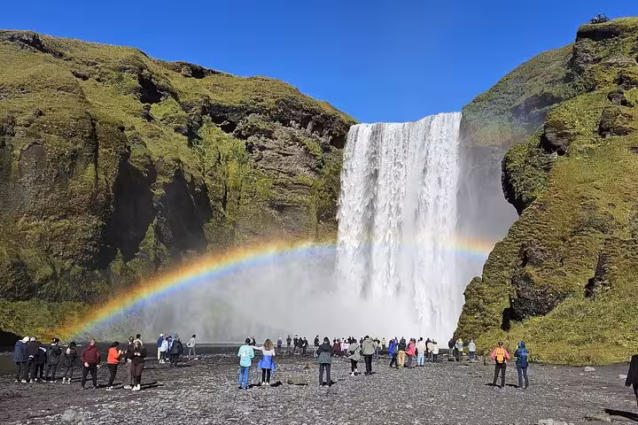 Tourists viewing Skógafoss waterfall with rainbow on Iceland South Coast day trip