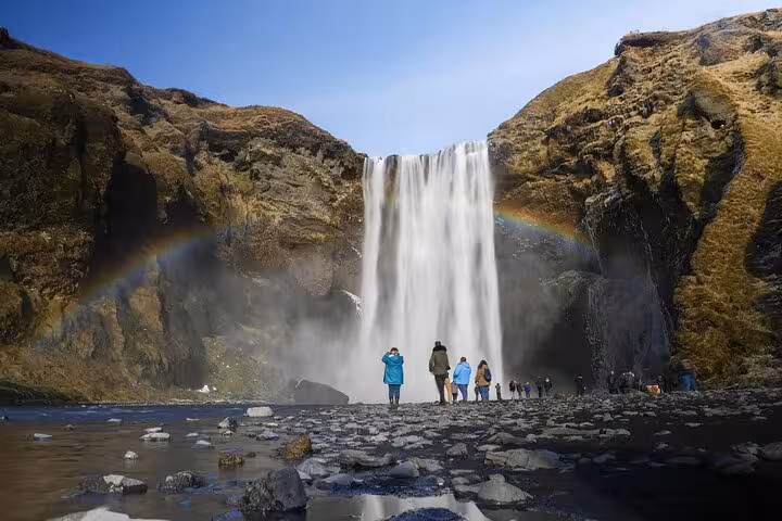 Tourists standing before Skógafoss waterfall with rainbow on Iceland's South Coast
