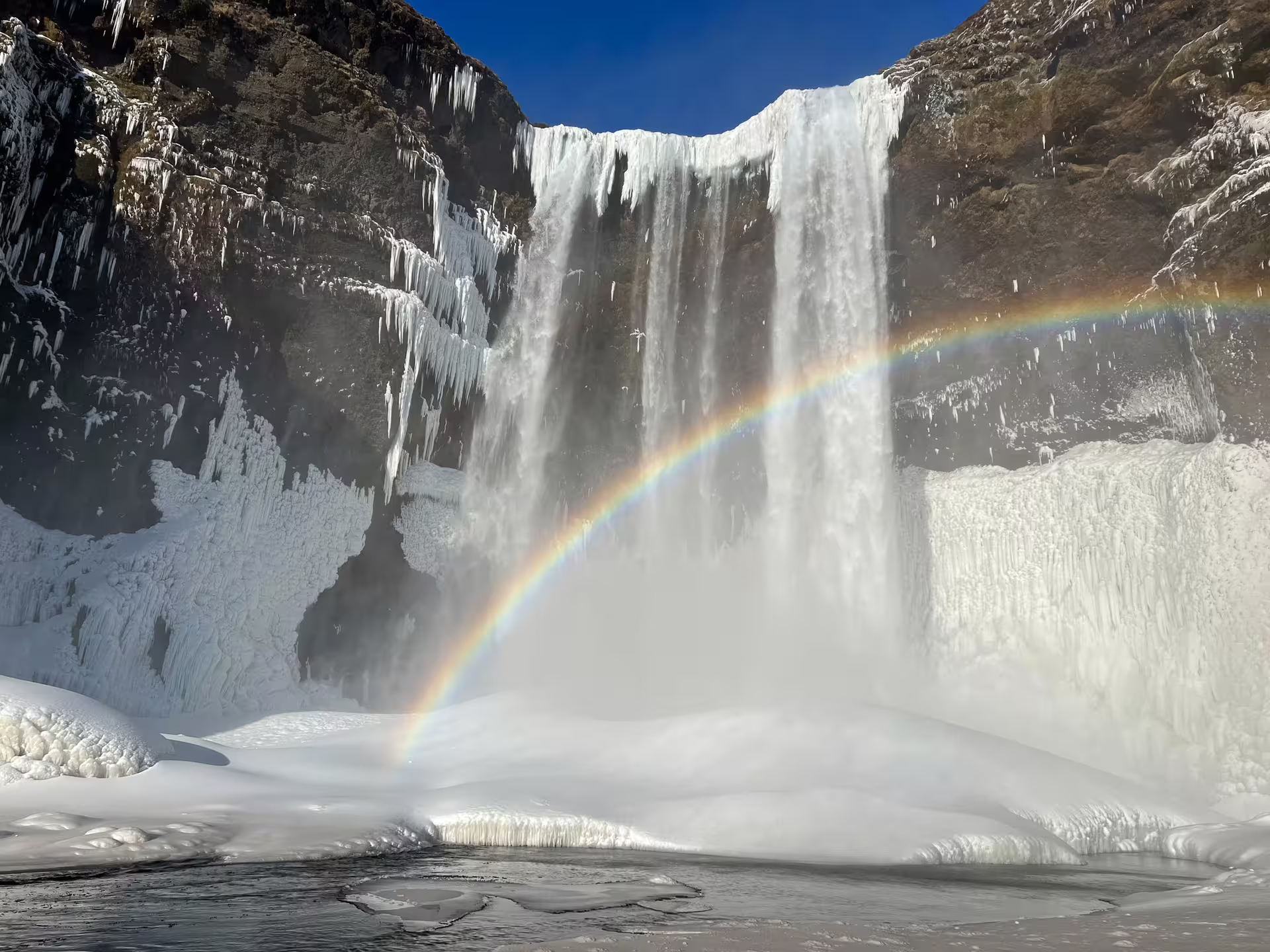 Skógafoss waterfall in winter with rainbow, surrounded by ice and snow on Iceland's South Coast