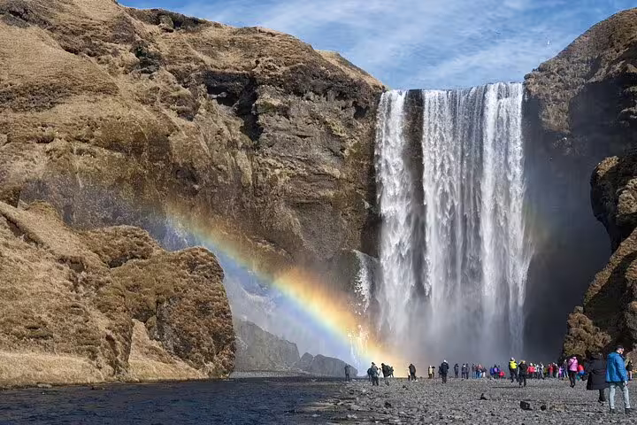 Skógafoss waterfall with rainbow and tourists on Iceland's south coast