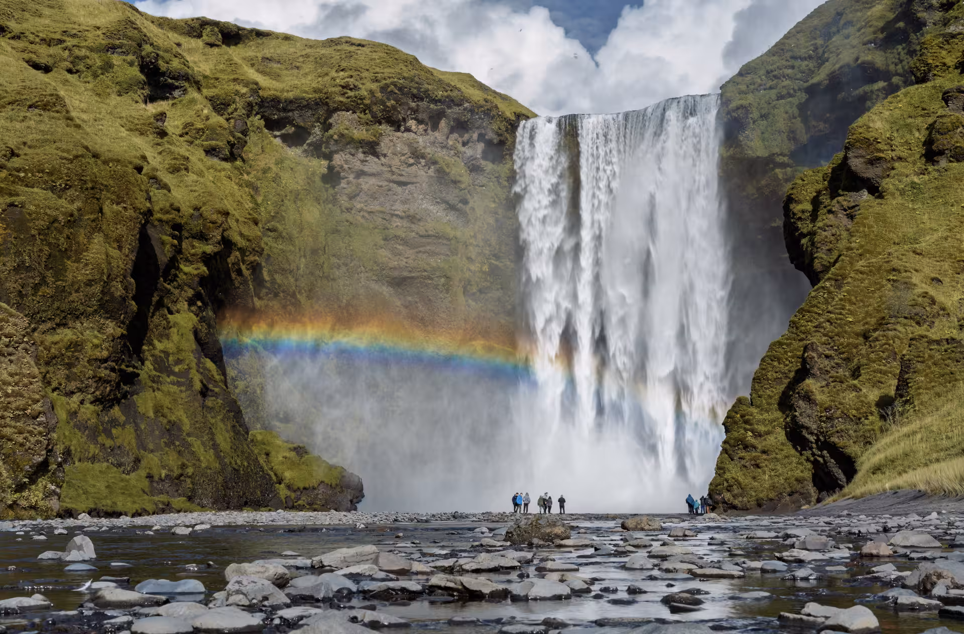 Skógafoss waterfall in Iceland with a vivid rainbow and tourists standing at its base