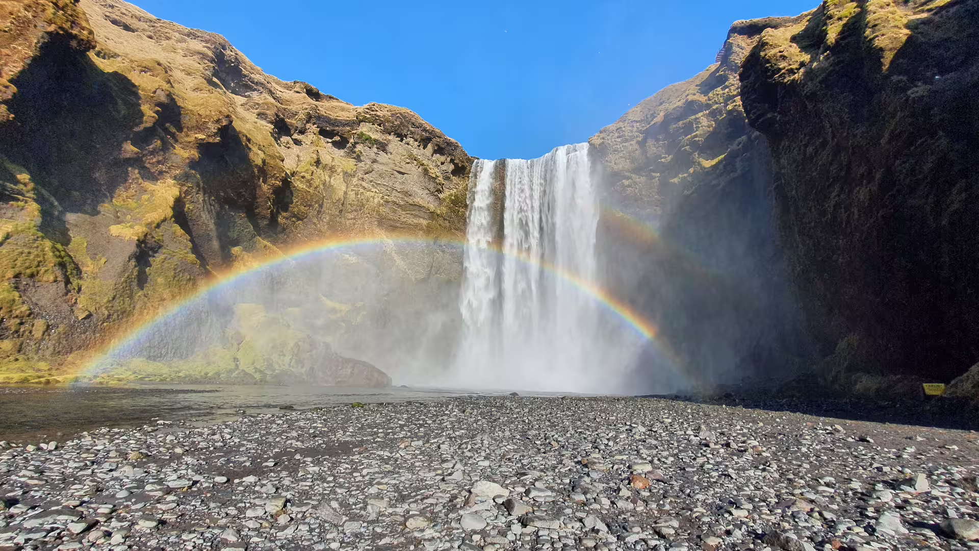 Skógafoss waterfall in South Iceland with a vivid double rainbow arching over rocky black beach