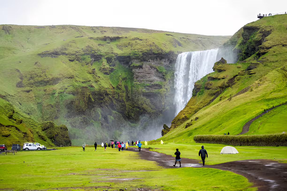 Tourists walking toward Skógafoss waterfall on Iceland's South Coast on a rainy day