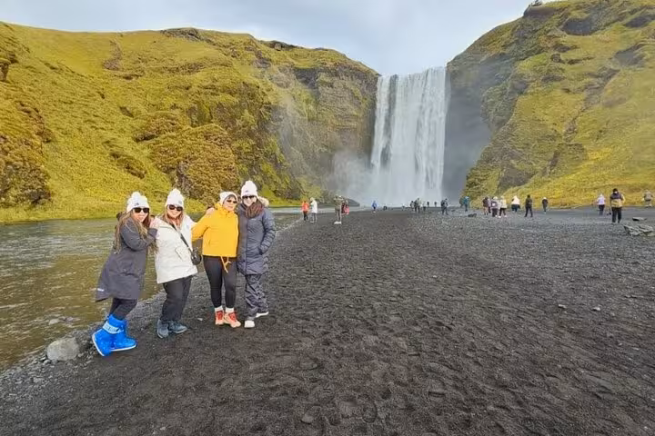 Four tourists posing at Skógafoss waterfall on Iceland's South Coast with black sand and green cliffs