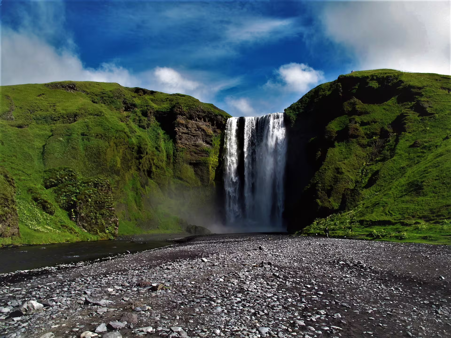 Skógafoss waterfall cascading down green cliffs on Iceland's south coast under a blue sky