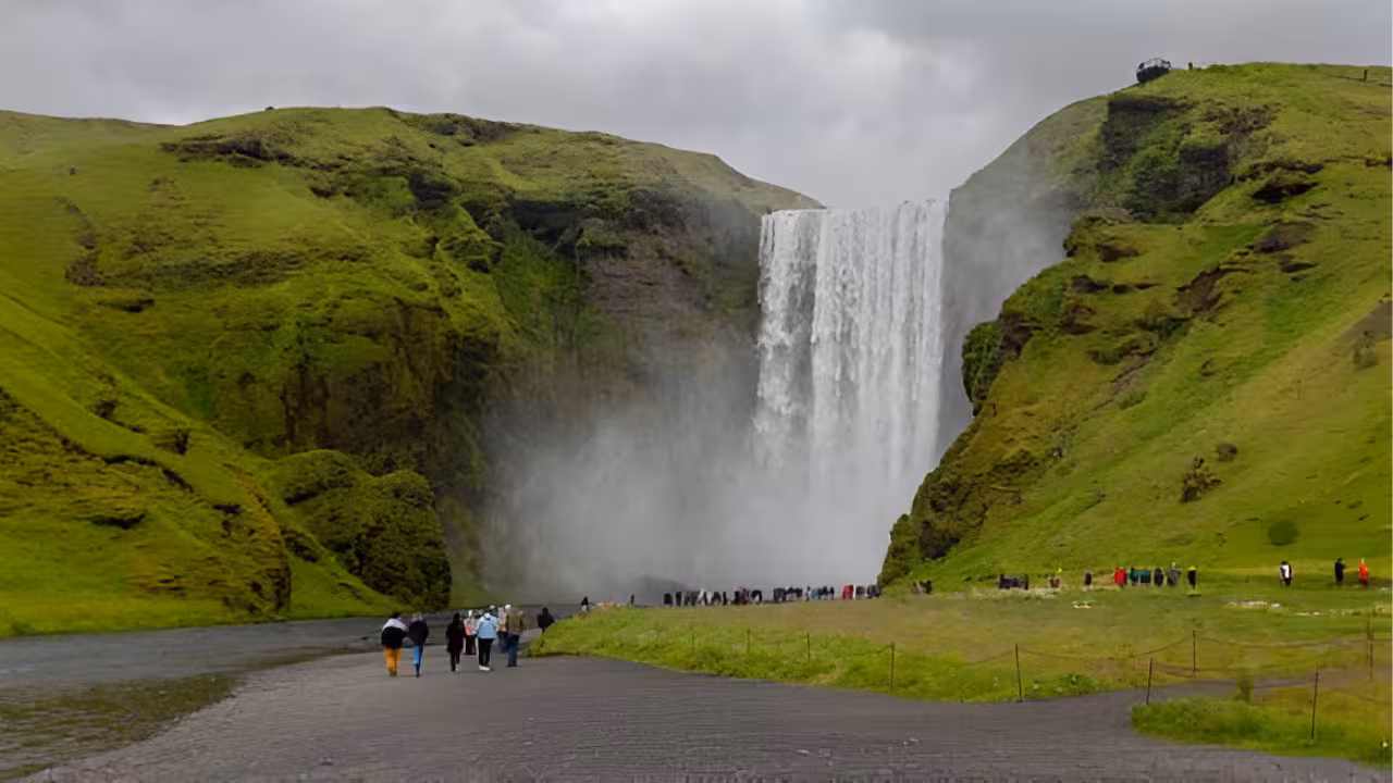 Tourists walking toward Skógafoss waterfall on Iceland's south coast on a cloudy day