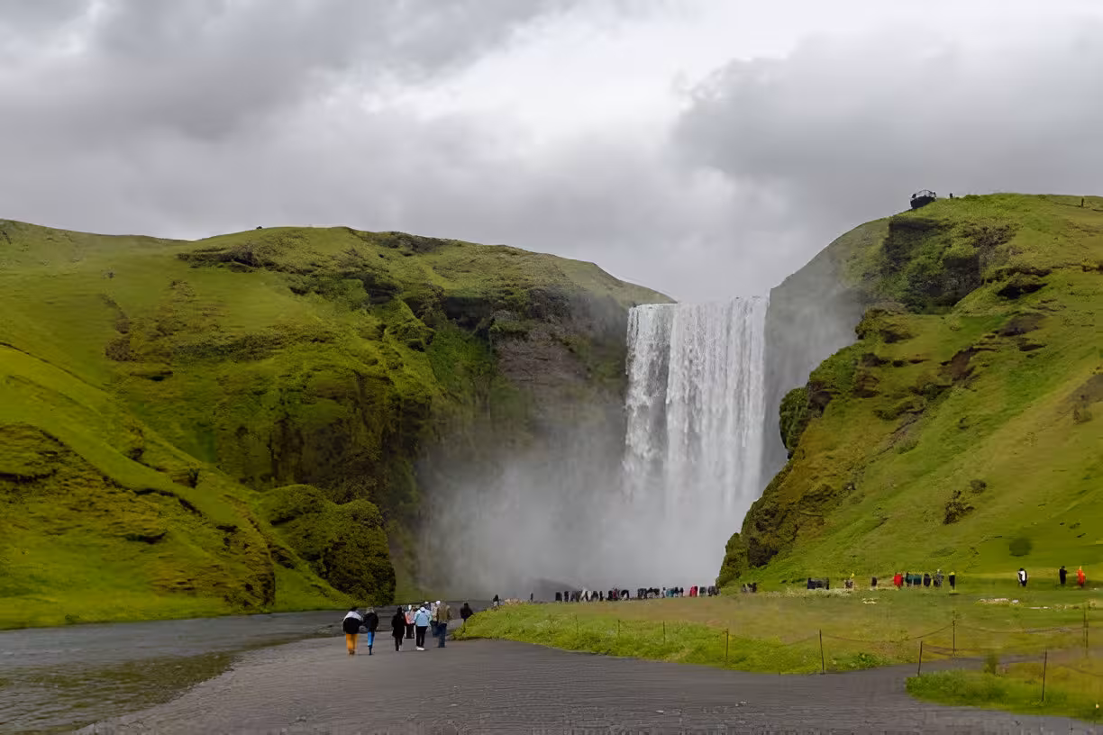 Tourists walking toward Skógafoss waterfall on Iceland's green south coast on a cloudy day