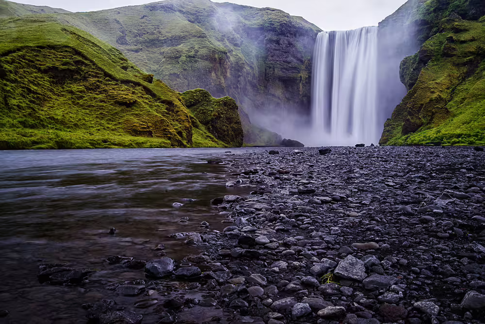 Skógafoss waterfall cascading into rocky river on Iceland's south coast surrounded by green cliffs