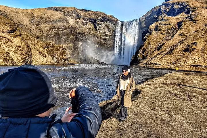 Tourist posing in front of Skógafoss waterfall on Iceland's South Coast on a sunny day