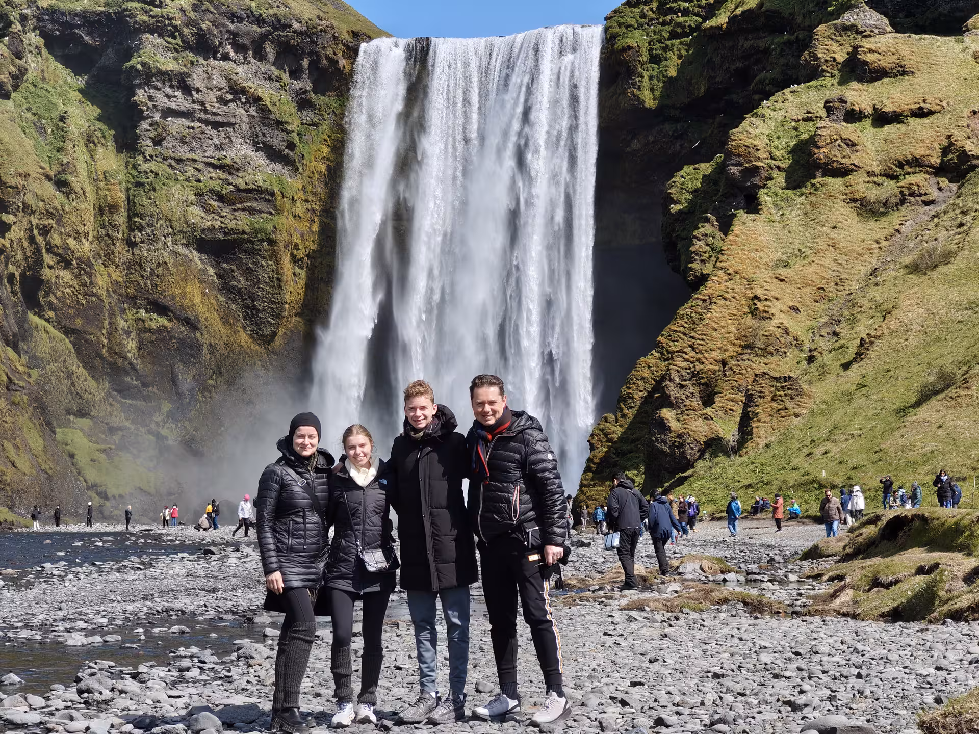 Family of four posing in front of Skógafoss waterfall on Iceland's South Coast on a sunny day
