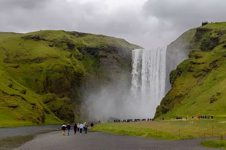 Tourists walking toward Skógafoss waterfall on Iceland's South Coast with lush green cliffs