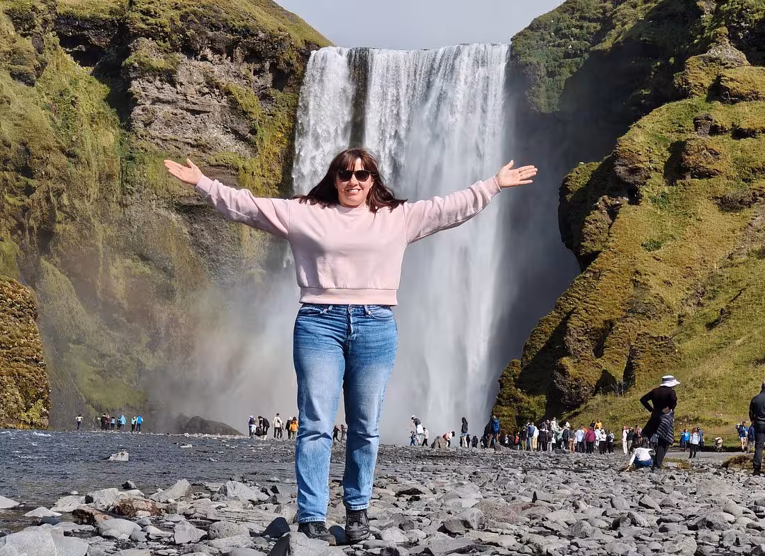Tourist posing with arms outstretched in front of Skógafoss waterfall on Iceland's South Coast