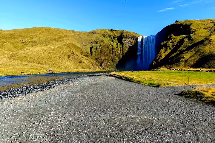 Skógafoss waterfall near Vík with green cliffs and black sand riverbed under blue sky, Iceland