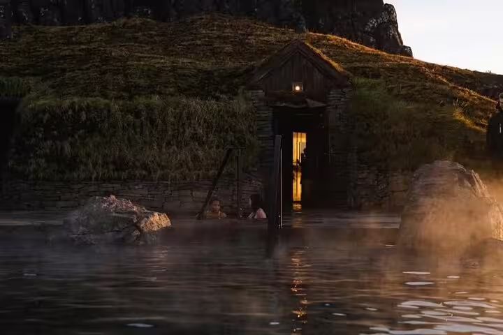 Steaming geothermal lagoon with rustic stone bathhouse entrance glowing at dusk in Iceland