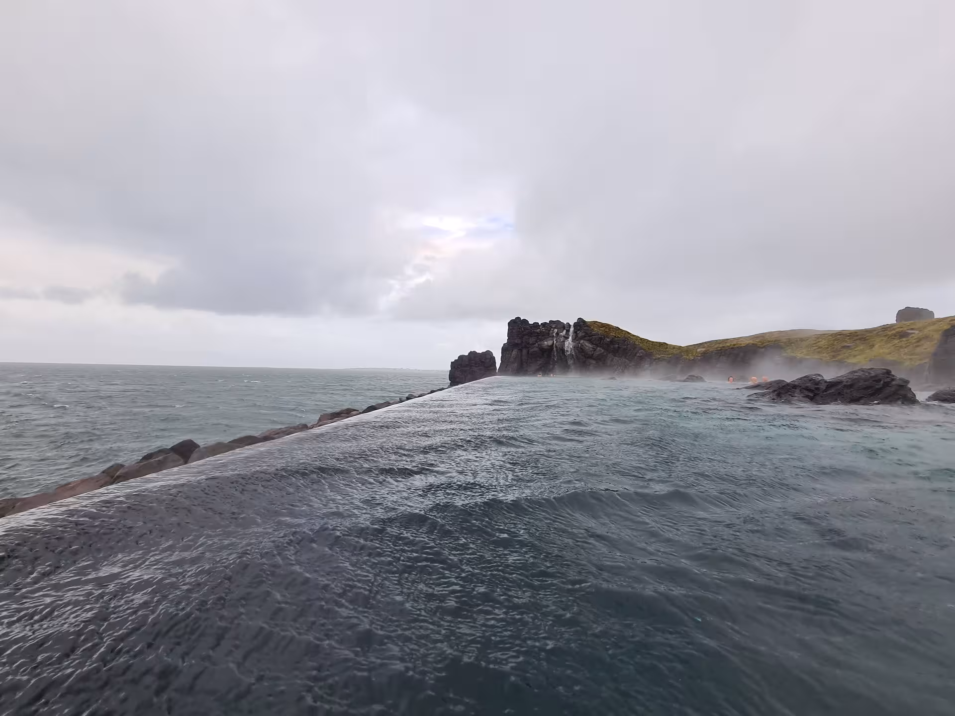 Steaming geothermal infinity pool merging with the ocean at Sky Lagoon, Iceland rocky coastline