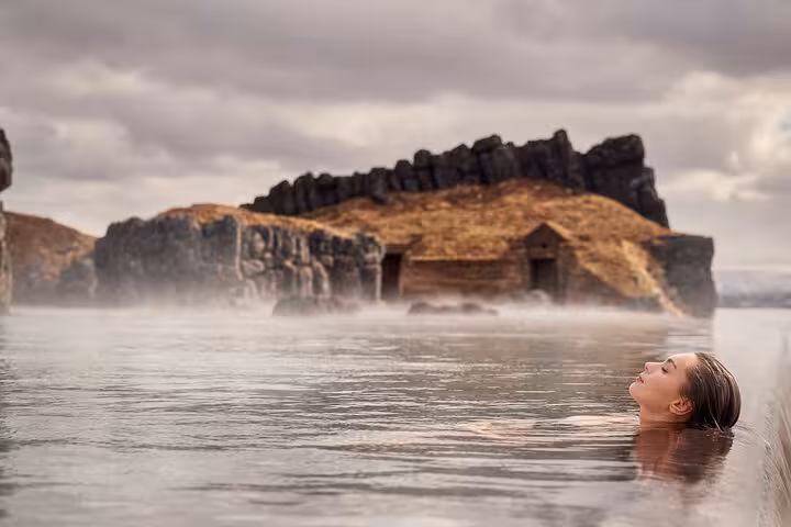 Woman relaxing in steaming geothermal waters of Sky Lagoon with dramatic volcanic rock formations in background