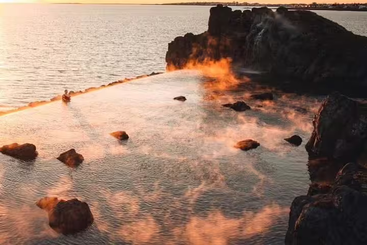 Sky Lagoon geothermal pool with steaming water surrounded by volcanic rocks at golden sunset