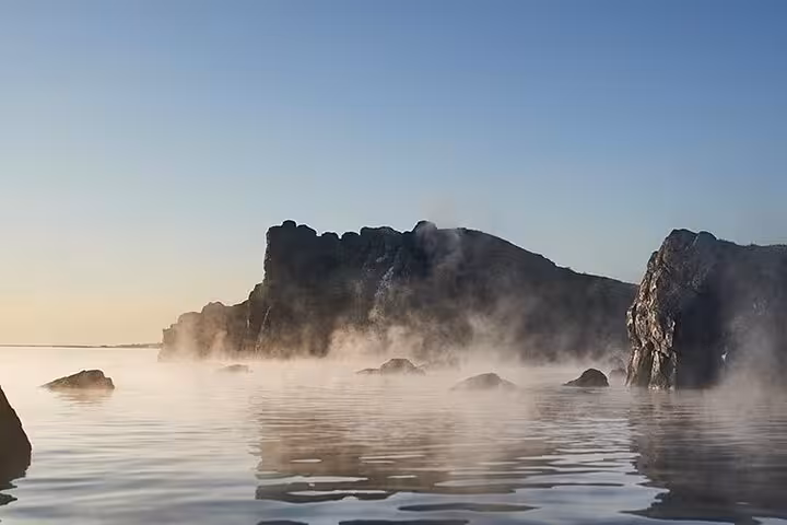 Misty volcanic rock formations rising from steaming geothermal waters at Sky Lagoon Iceland at sunrise