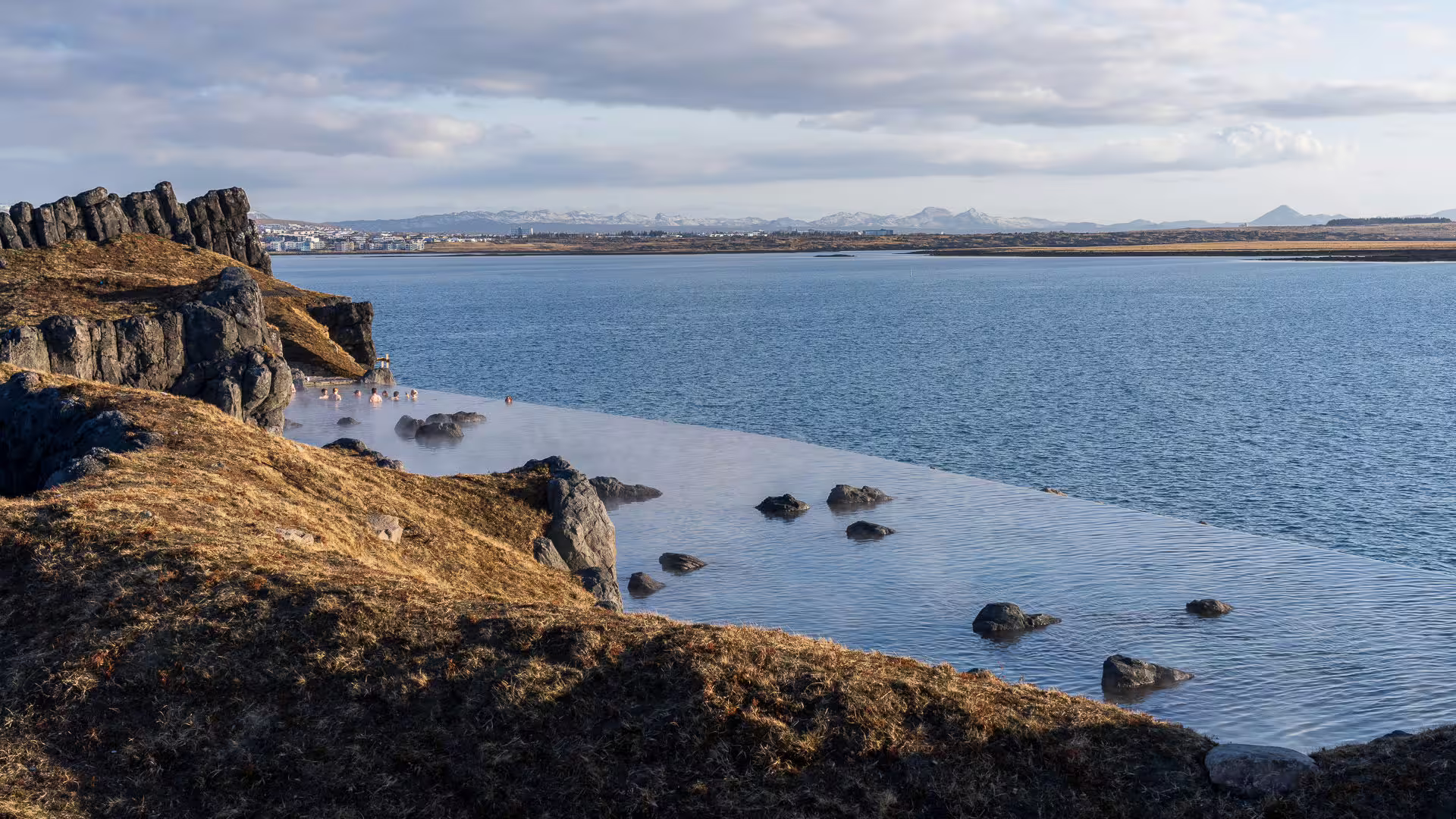 Sky Lagoon infinity pool overlooking Reykjavik fjord with snow-capped mountains in the background