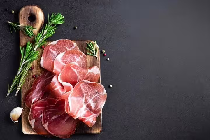 Sliced Parma ham elegantly arranged on a wooden board with rosemary, highlighting Italian gourmet cuisine.