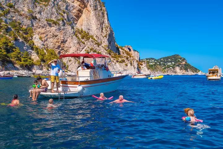 Group swimming and relaxing near a boat along the Capri coastline during a small group excursion from Sorrento.