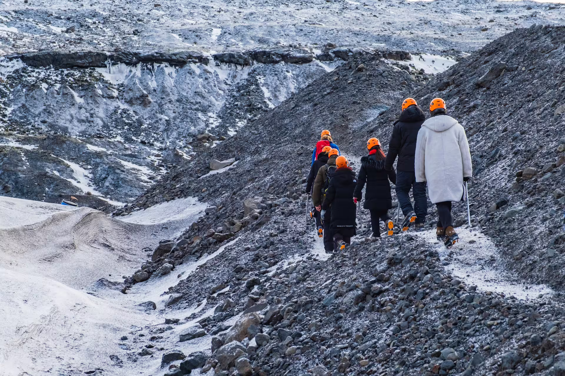 Group of hikers with orange helmets and trekking poles walking on Solheimajokull glacier in Iceland