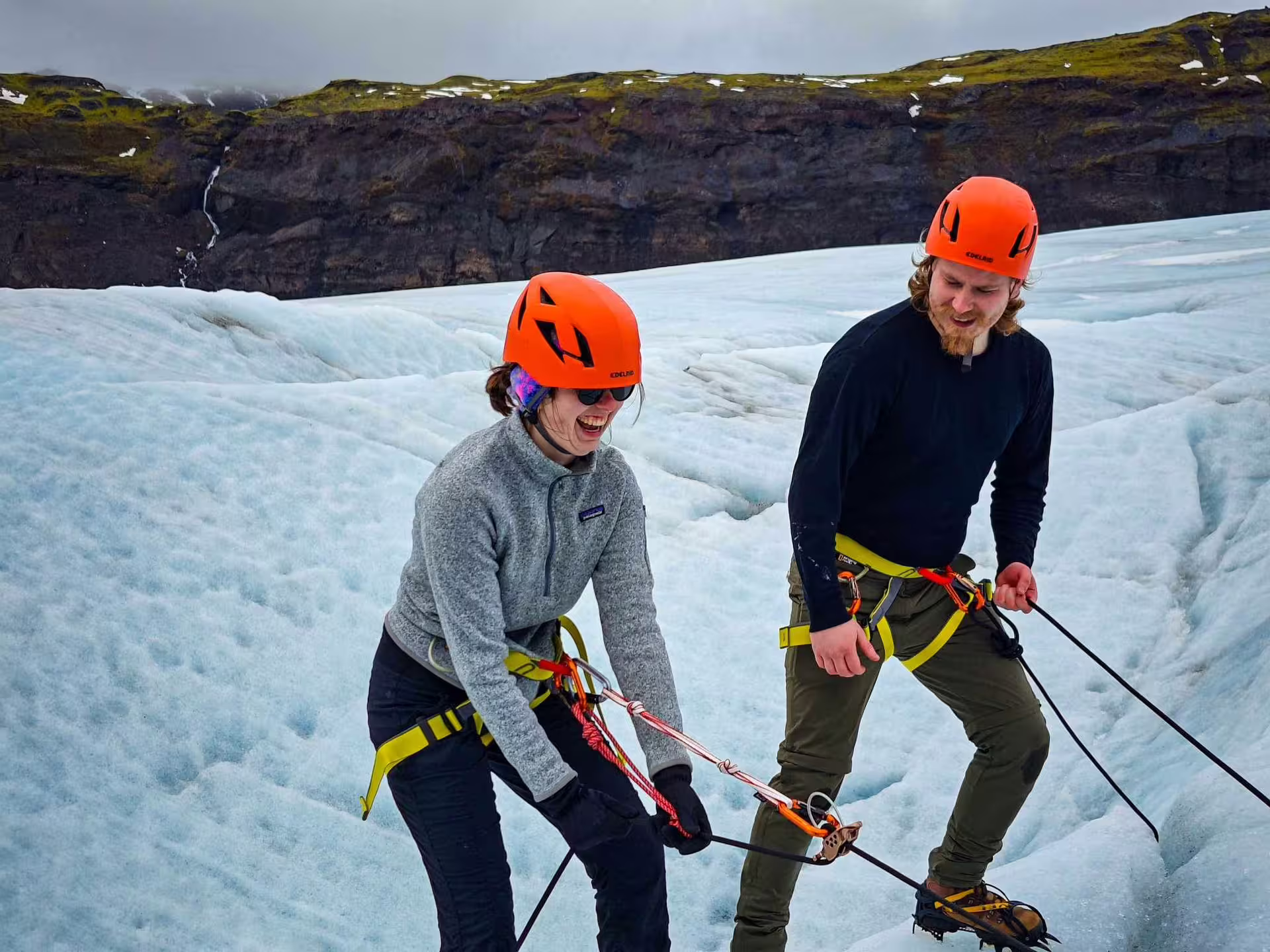 Two hikers in orange helmets and harnesses glacier hiking on Solheimajokull glacier in Iceland