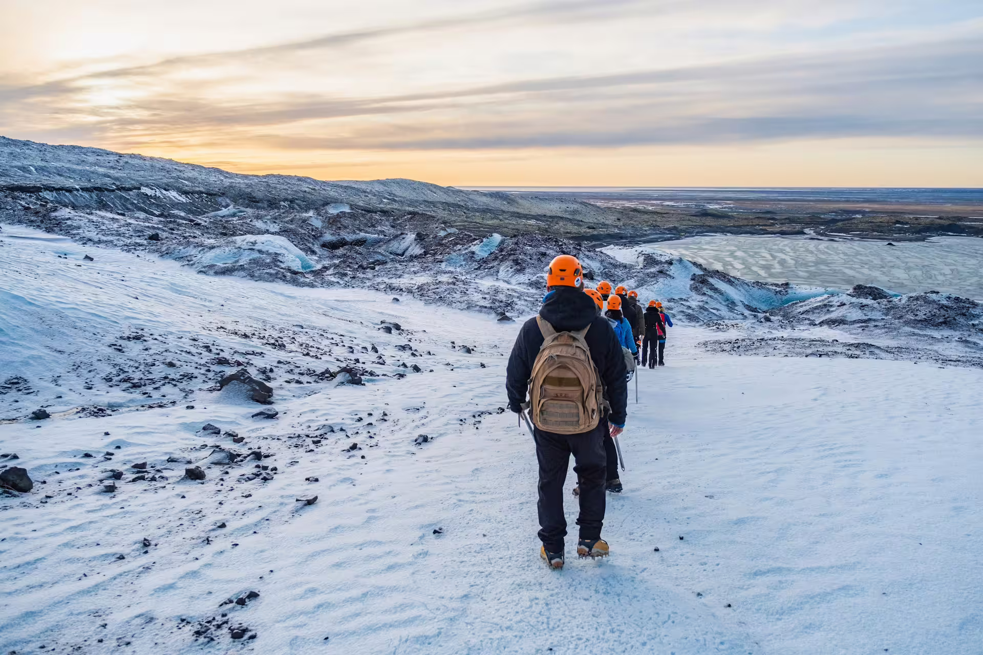 Group of hikers with orange helmets walking across Solheimajokull glacier at sunset in Iceland