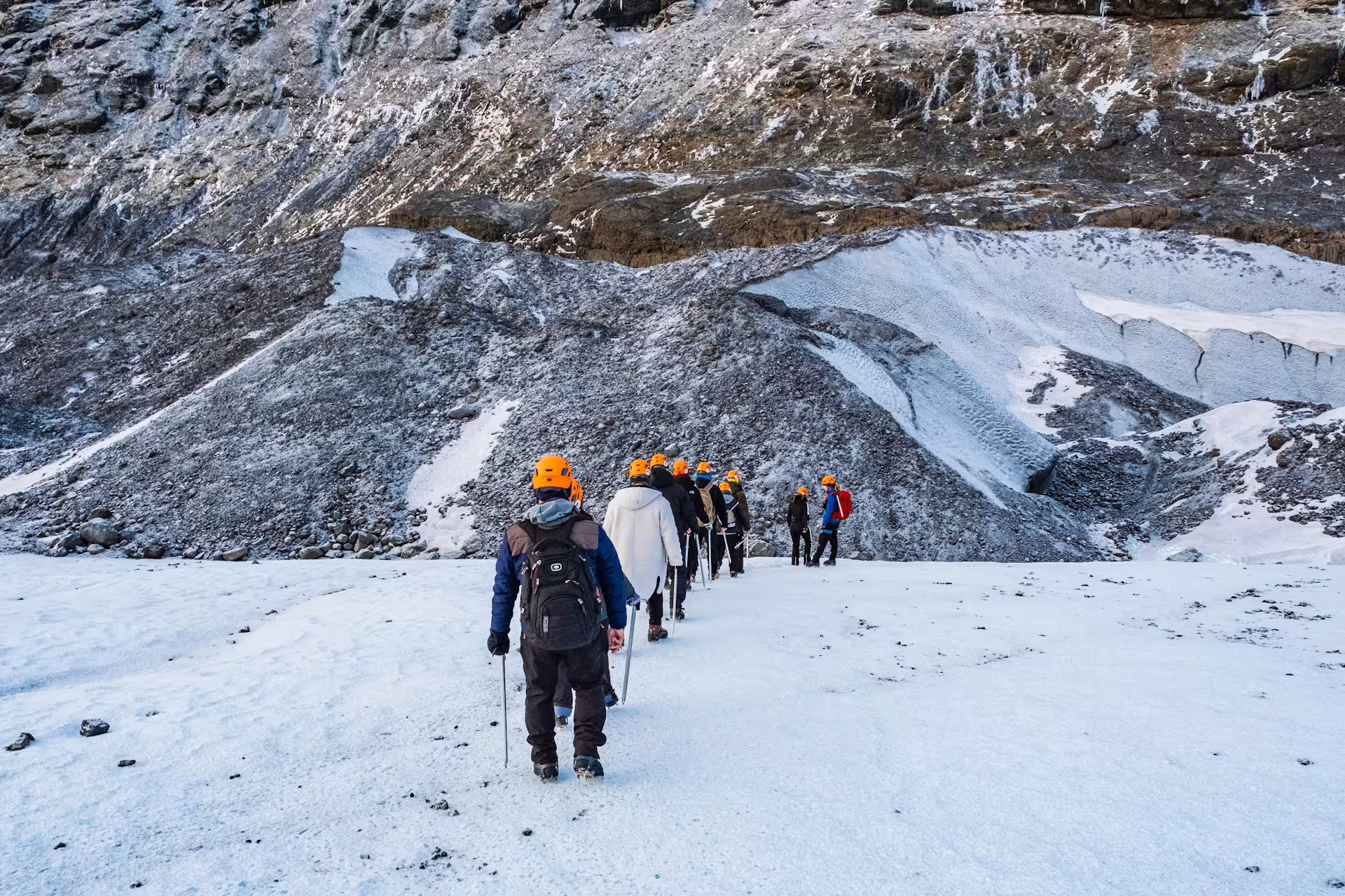 Group of hikers in orange helmets trekking across Solheimajokull glacier in Iceland