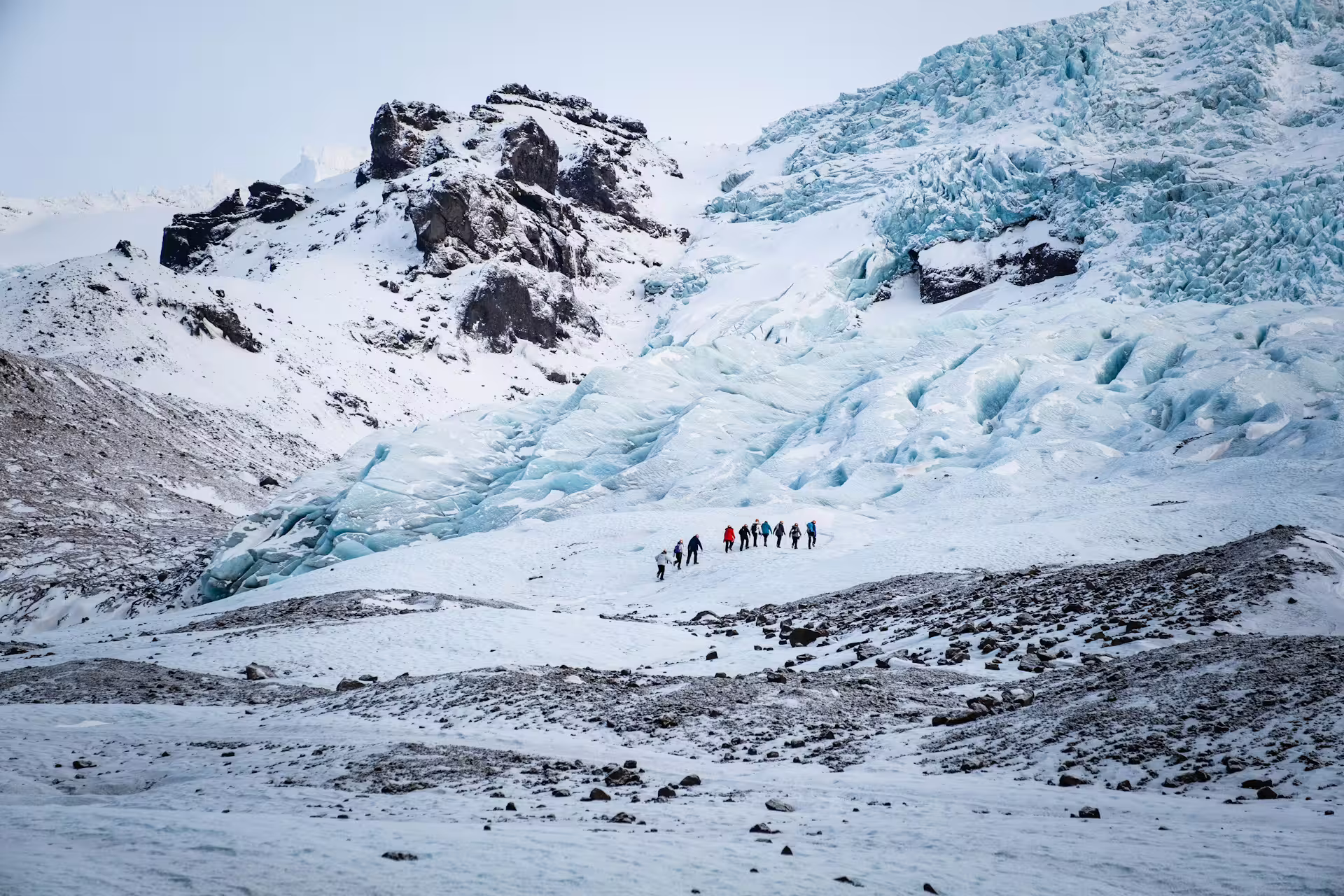 Small group of hikers trekking across Solheimajokull glacier with blue ice formations in Iceland
