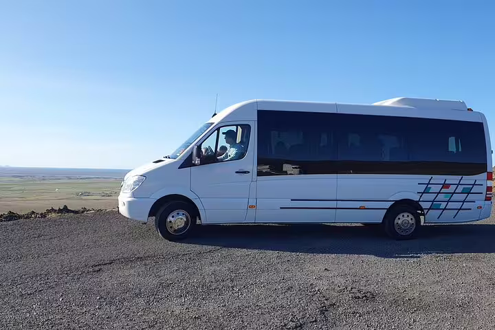 White Mercedes minibus for small group Golden Circle tour parked on gravel road with Icelandic landscape