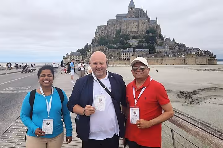 Small group Mont Saint Michel day trip guests posing on causeway with abbey backdrop, luxury van tour