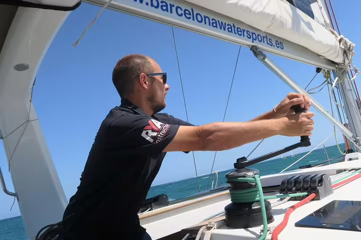 Man operating a sailboat winch on a sunny day during a 2-hour small group cruise with food and drinks, Barcelona coast.