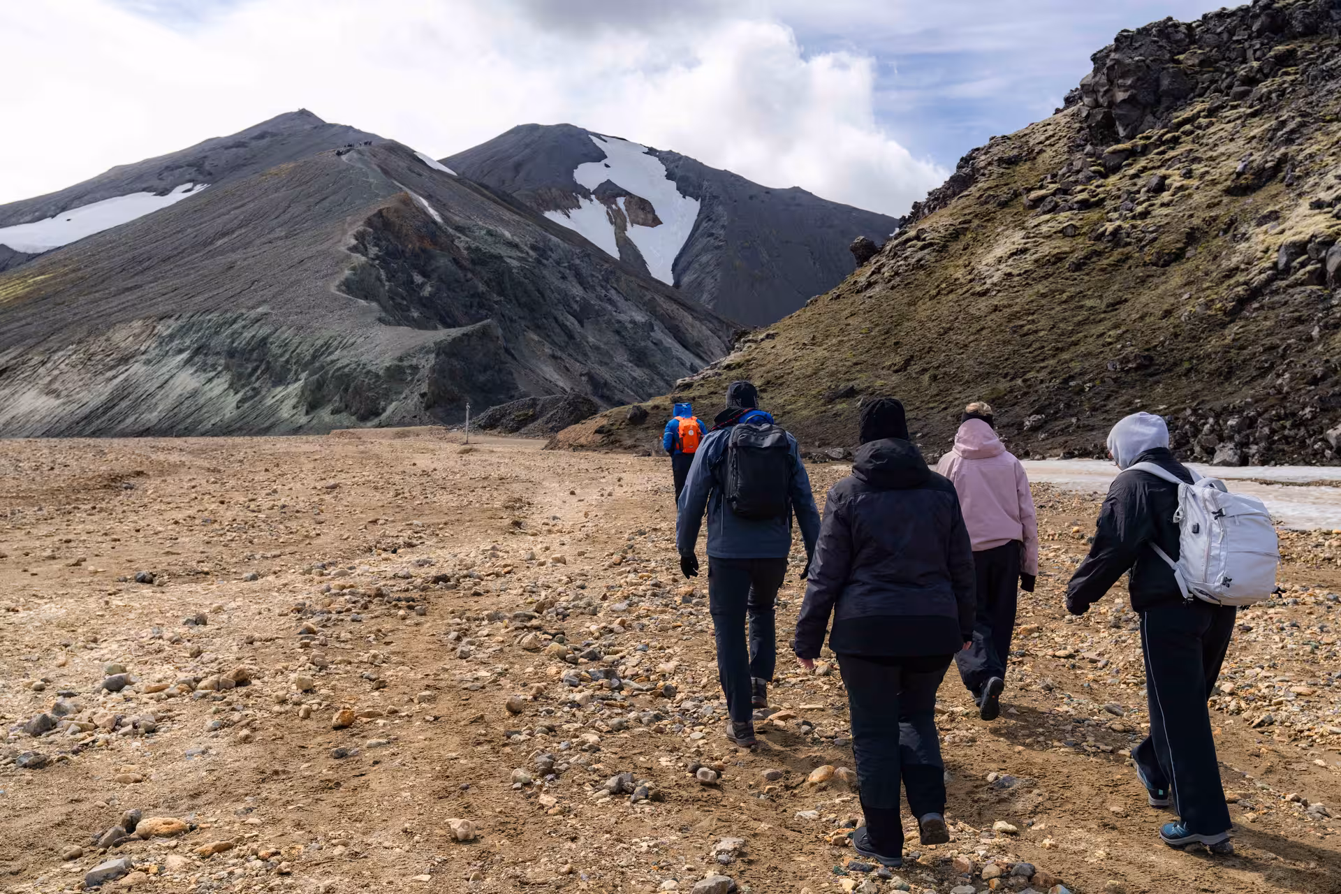 Group of hikers trekking across rocky terrain toward volcanic highlands of Landmannalaugar, Iceland
