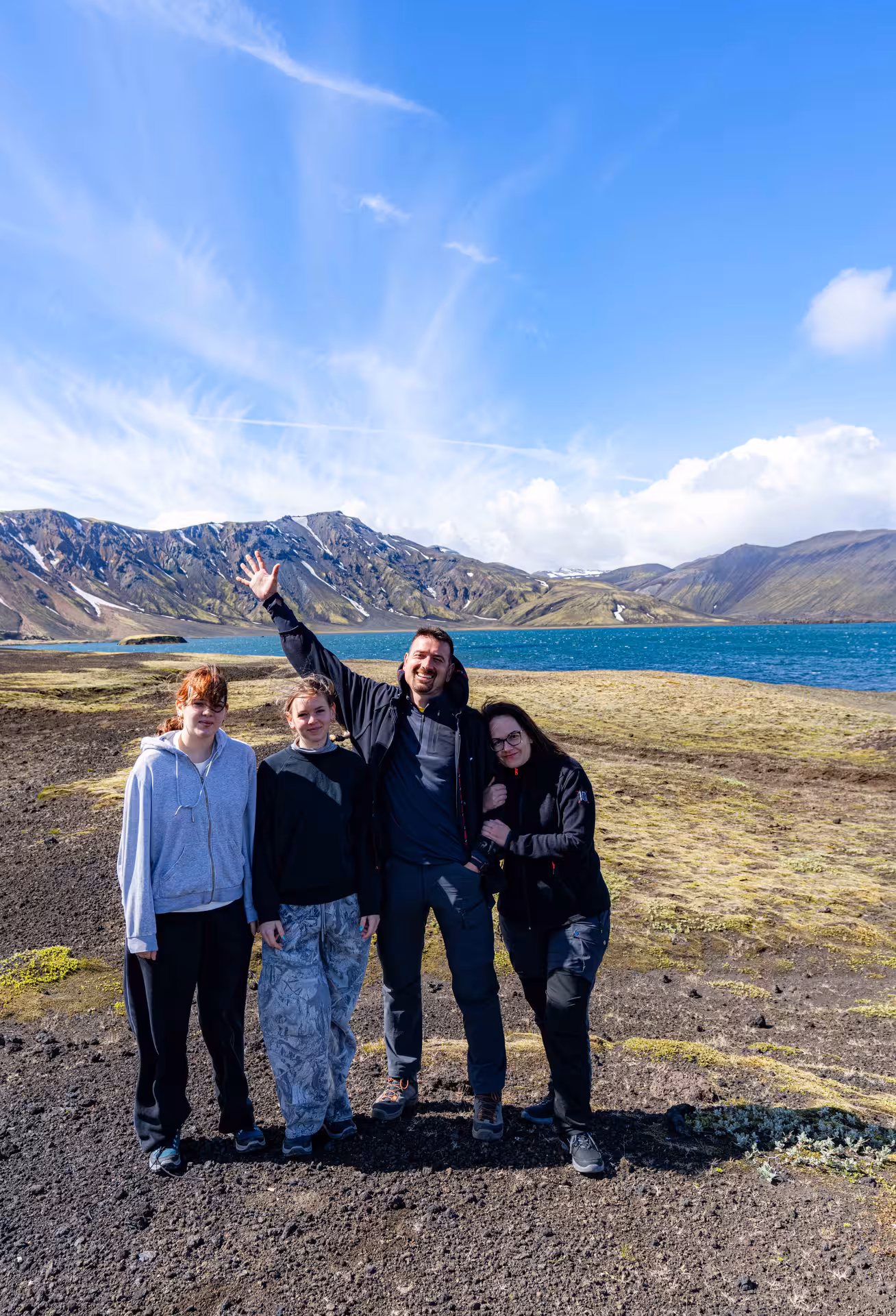 Group of four tourists posing by turquoise lake with snow-capped mountains at Landmannalaugar Highlands